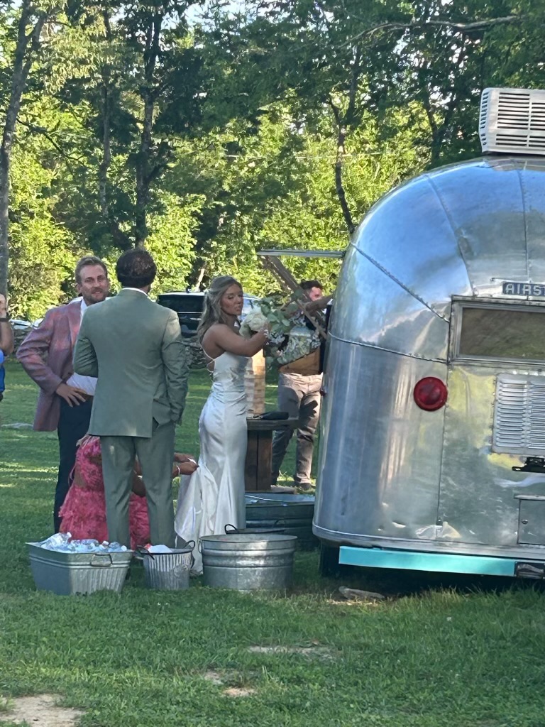 The bride and guests celebrating by the Airstream Bambi bar on the lawn