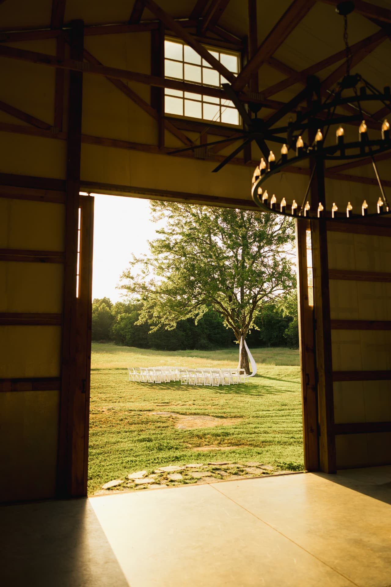 Wagon-wheel chandeliers inside the barn looking out to the ceremony lawn